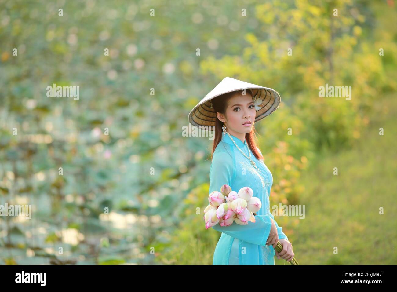 Porträt einer schönen Frau in einem traditionellen konischen Hut mit einem Strauß Seerosenblumen, Thailand Stockfoto