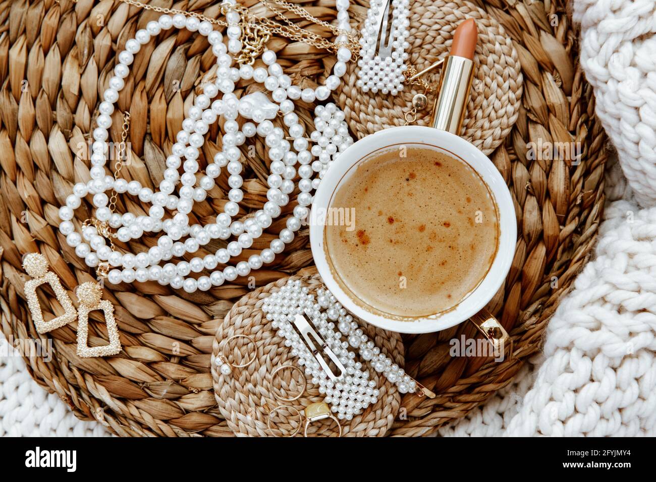 Tasse Kaffee mit Ringen, Ohrringen, Halsketten, Lippenstift und Haarclips Stockfoto