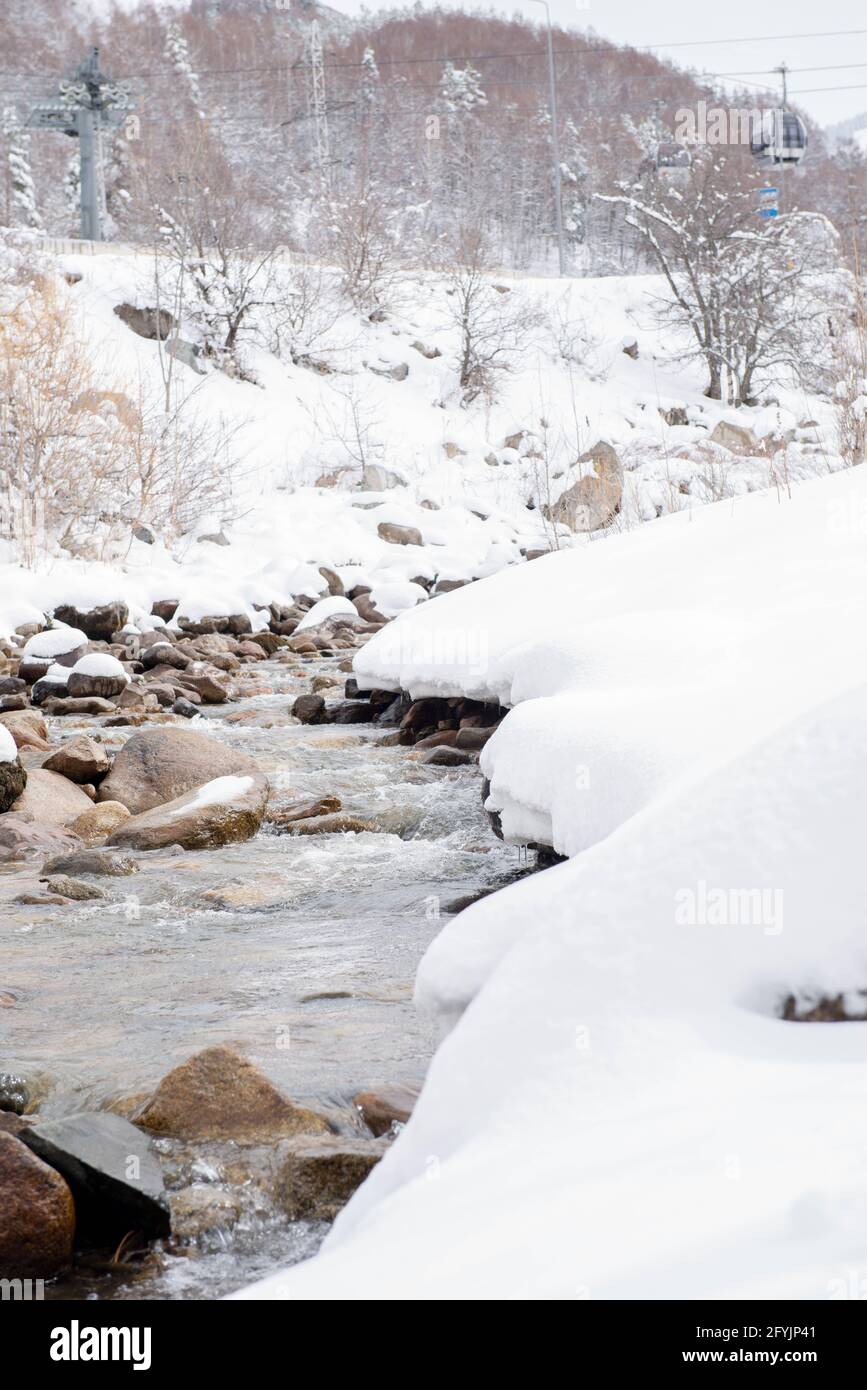 Berge und Gebirgsfluss mit Steinen im Schnee Stockfoto