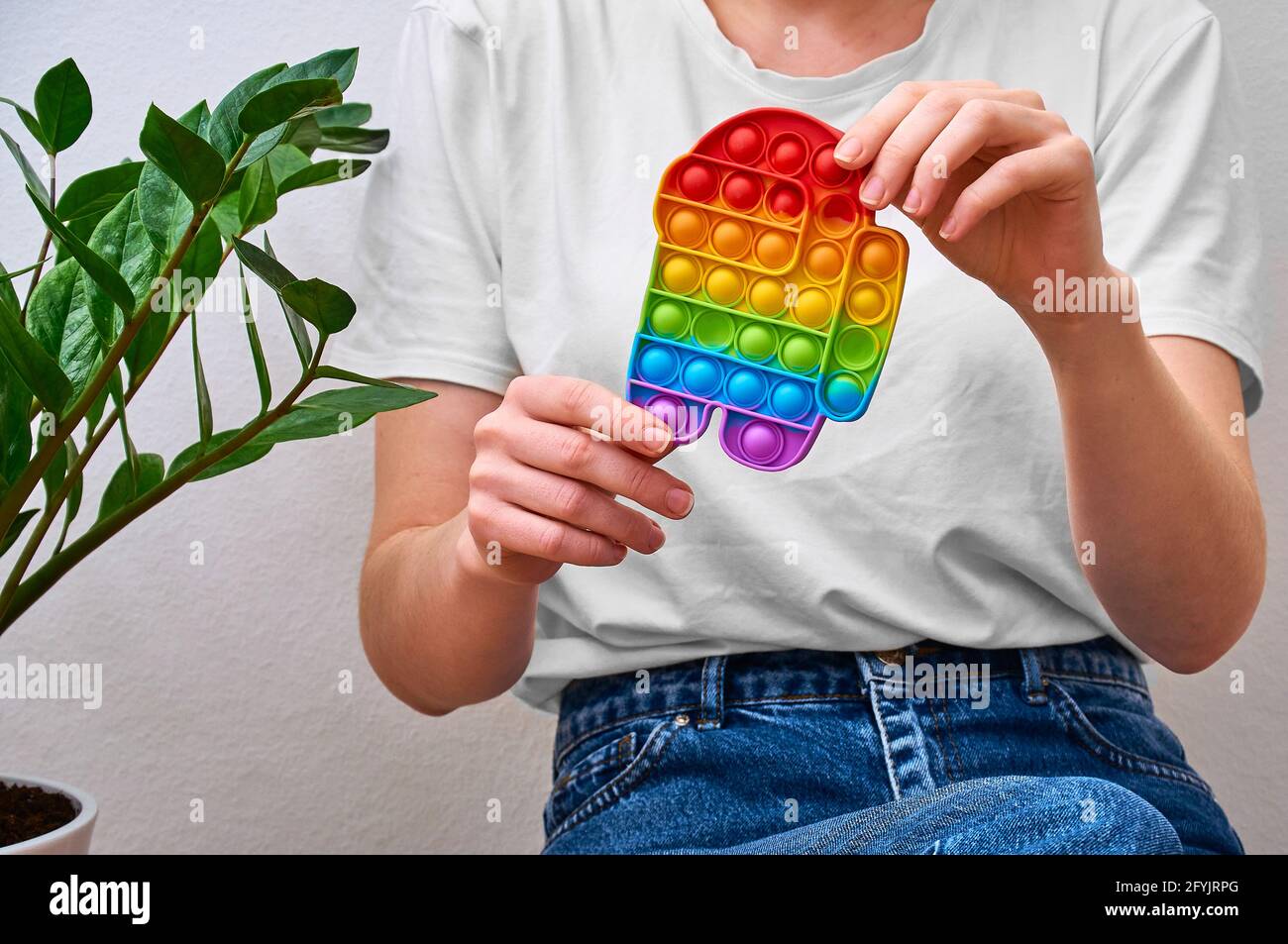 Close-up Mädchen in den Händen halten bunte trendige Pop-it-Spielzeug in Form eines Charakters unter uns. Stockfoto