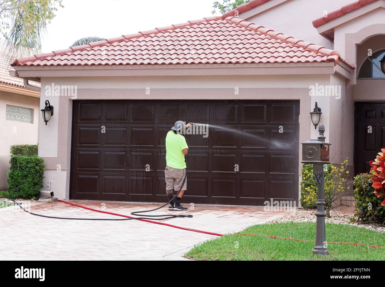 Mann macht waschen ein Garagentor in Florida. Der Hochdruckstreay entfernt Schmutz, Schlamm, Moos, Schimmelsporen, Flechten, Und Algen. Stockfoto