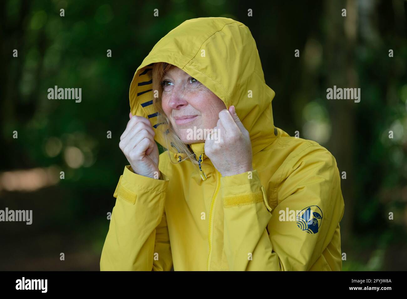 Eine Frau in einem gelben Regenmantel mit Kapuze, die in die Ferne blickte, saß auf einer Bank im Wald. Stockfoto