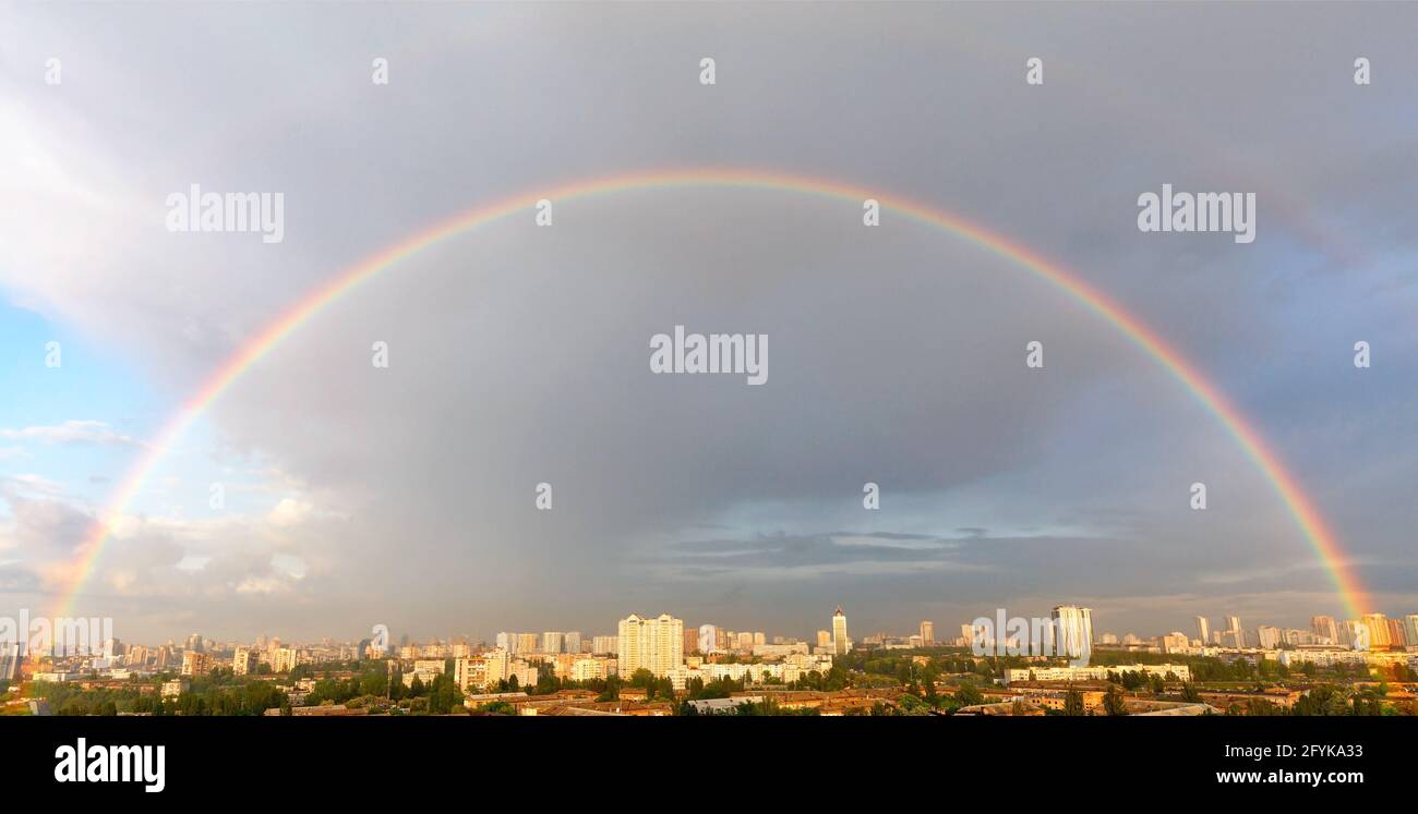 Ein großer Halbkreis eines schönen Regenbogens in Sonnenlicht über dem Panorama eines städtischen Wohngebiets. Stockfoto