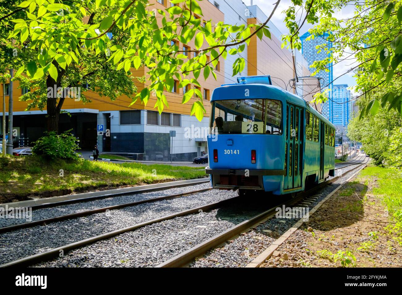 Moskau. Russland. 24.Mai 2021. Die blaue Straßenbahn fährt durch den Stadtpark. Sommersonntag und grünes Laub von Bäumen. Stockfoto