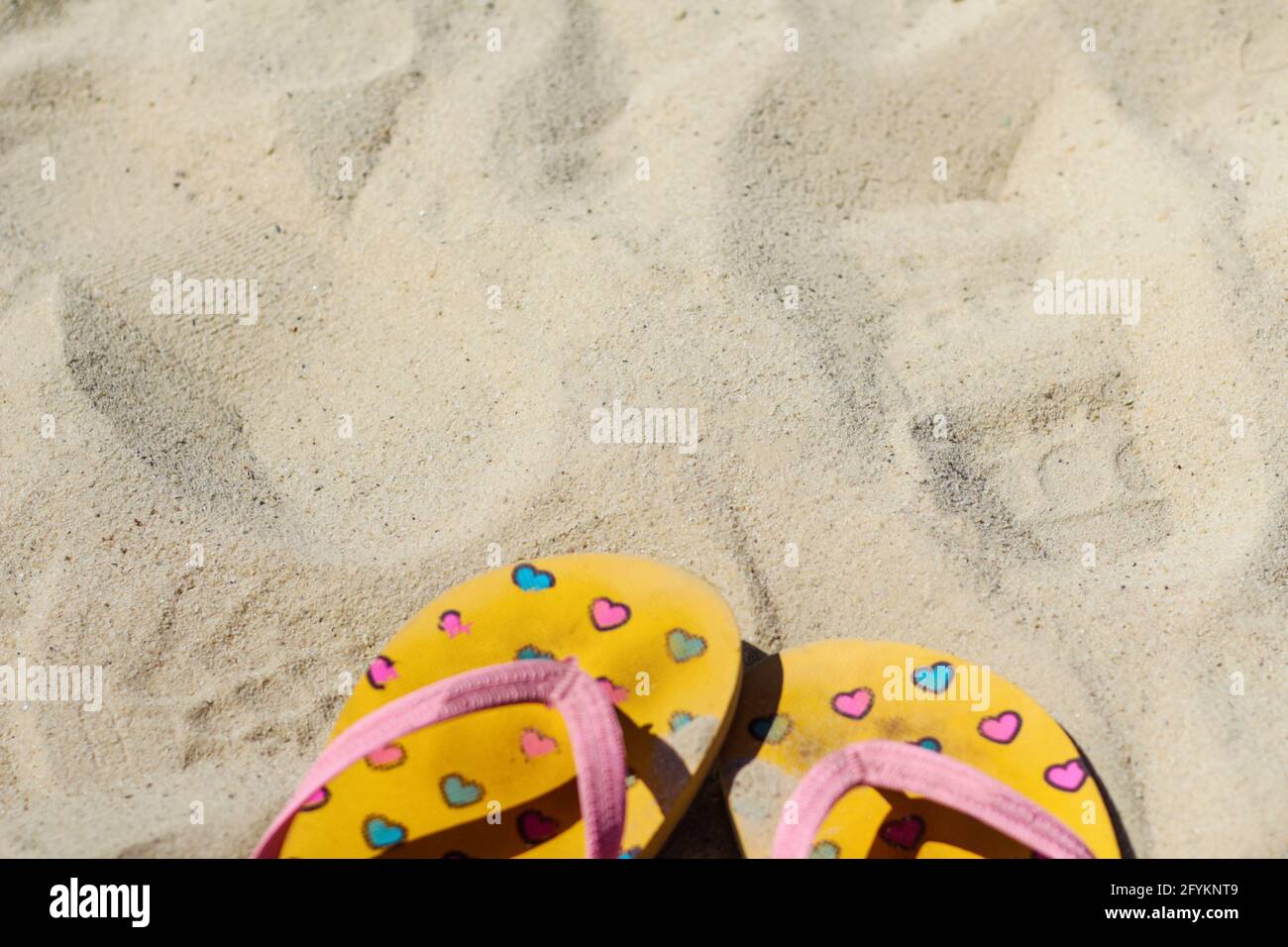 Unschärfe-Flipflops in hellem Gelb und Rosa mit pinken und blauen Herzen auf dem Sand. Sommer Hintergrund.das Konzept von Wärme, Entspannung und Erholung Stockfoto