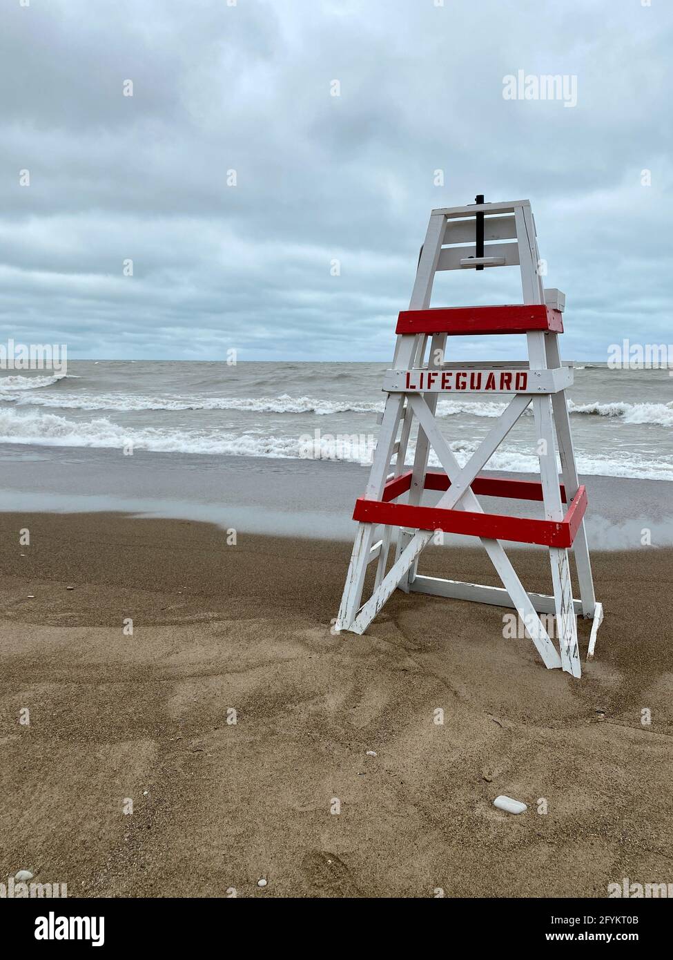 Leerer Rettungsschwimmerstuhl am Tower Beach an der Küste von Lake Michigan in Illinois an einem stürmischen Tag, an dem die Wellen im Hintergrund am Ufer entlang krachen. Stockfoto