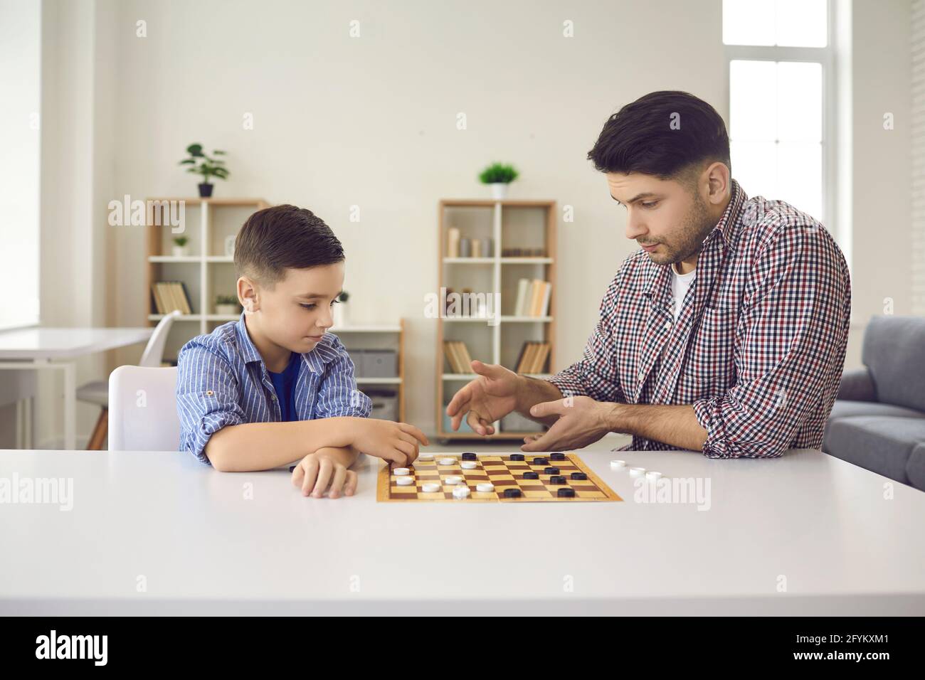 Porträt von konzentriertem Vater und Sohn spielen Dame sitzen an Starttisch Stockfoto