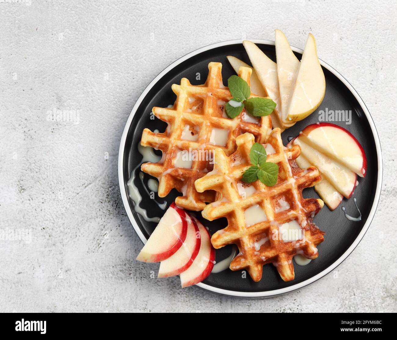 Wiener Waffeln serviert mit Früchten auf einem runden Teller auf hellgrauem Hintergrund. Draufsicht, flach liegend Stockfoto