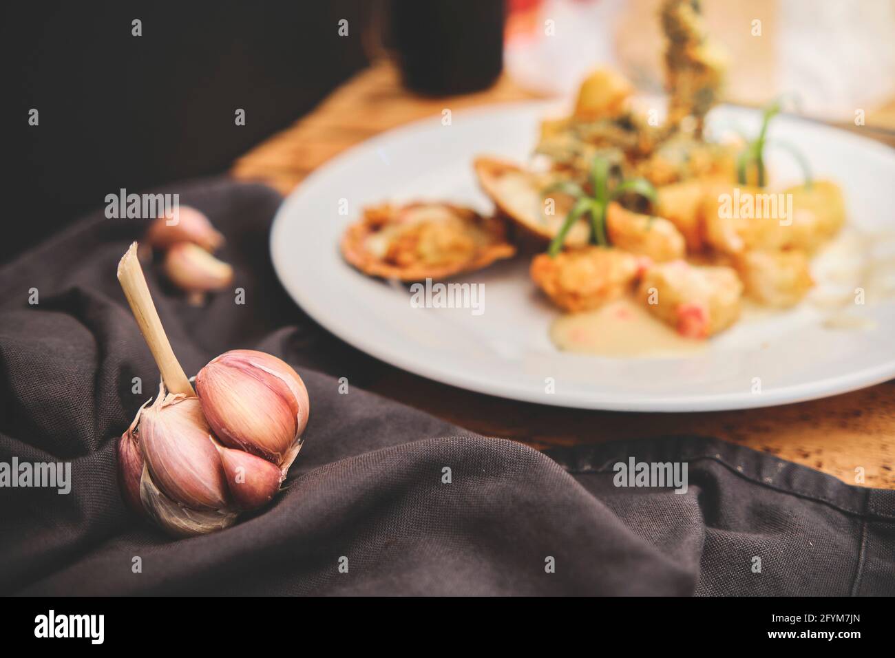 Peruanische Küche: Sautierte Garnelen mit Kräutern und Knoblauch, Holztisch, serviert auf einem weißen Teller, begleitet von purpurem Maissaft Stockfoto