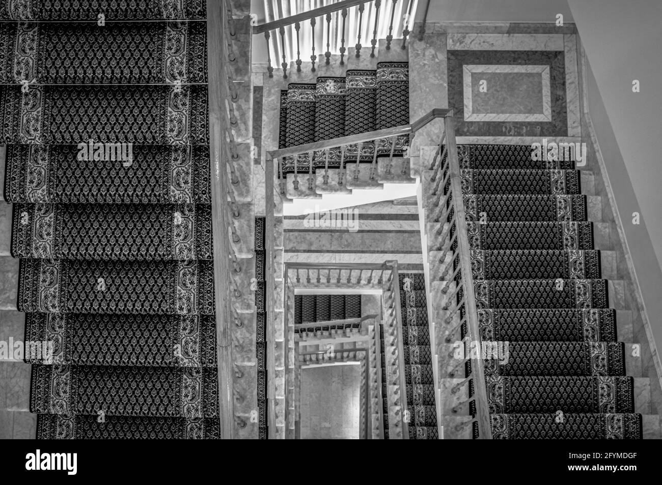 Blick nach unten auf eine Wendeltreppe mit mehreren, mit Teppichen geschmückten Flügen. Schwarz und Weiß. Stockfoto