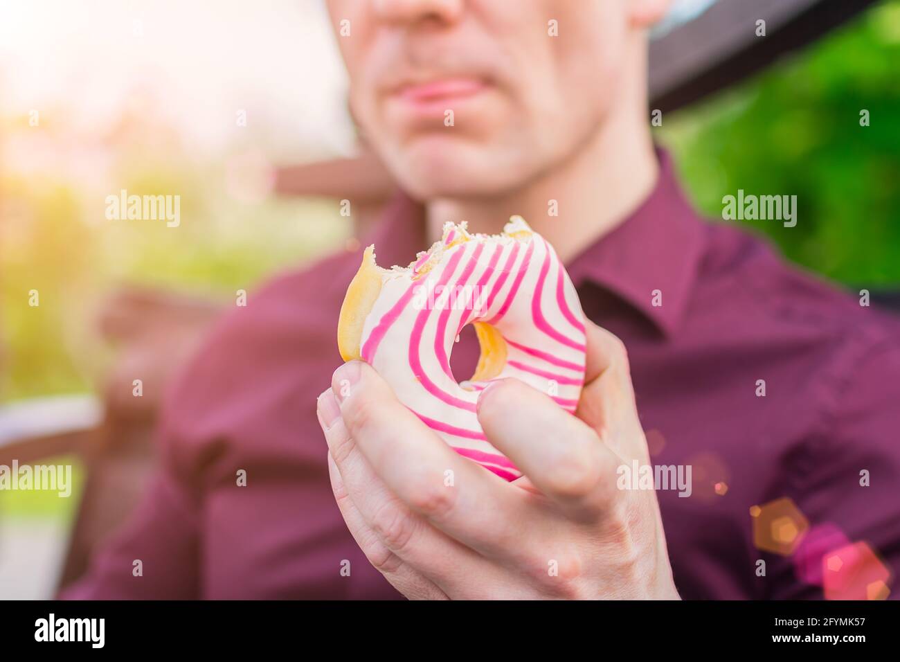 Nahaufnahme von köstlichem glasierten Donut in den Händen eines Büromitarbeiters während des Mittagessens im Freien Stockfoto