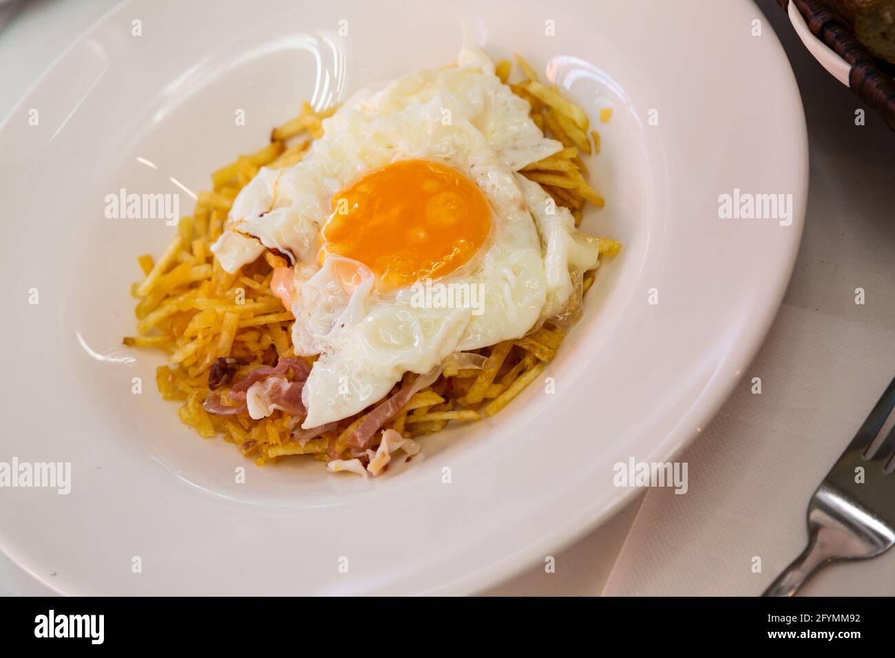 Traditionelles, appetitliches spanisches Mittagessen - Spiegelei mit pommes frites Und Scheiben von Jamon auf weißem Teller Stockfoto