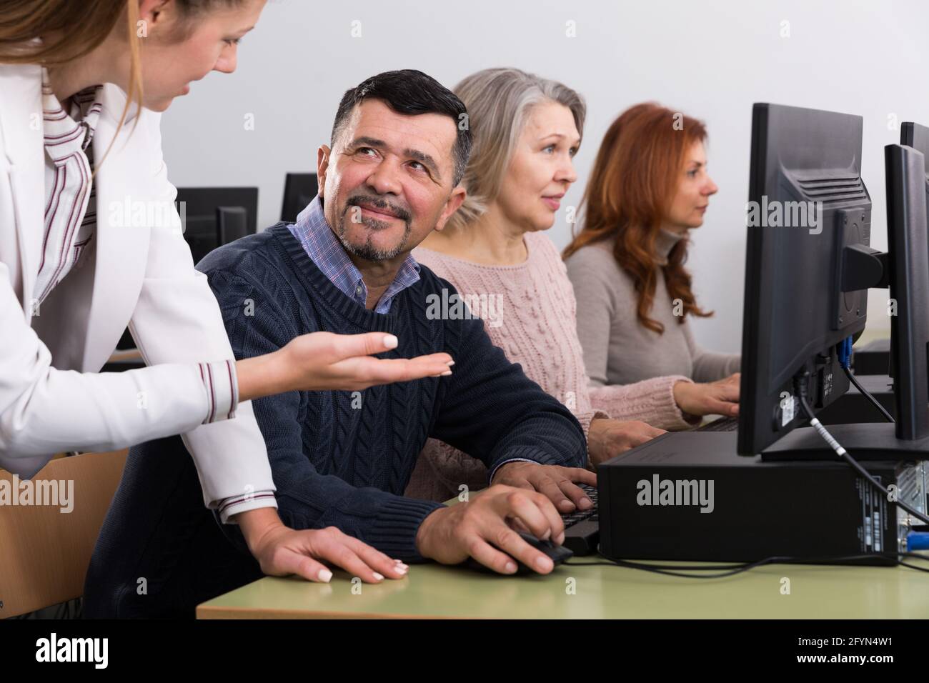 Junge weibliche Lehrer erklären, Computerkenntnisse zu reifer Mann in der Klasse Stockfoto