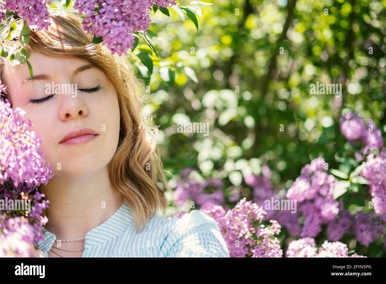 Ehrliches, authentisches Porträt einer kaukasischen blonden Frau aus den 30er Jahren mit Fliederblumen. 30 40-jährige Frau genießen das Leben in lila Blumen Natur Hintergrund Stockfoto