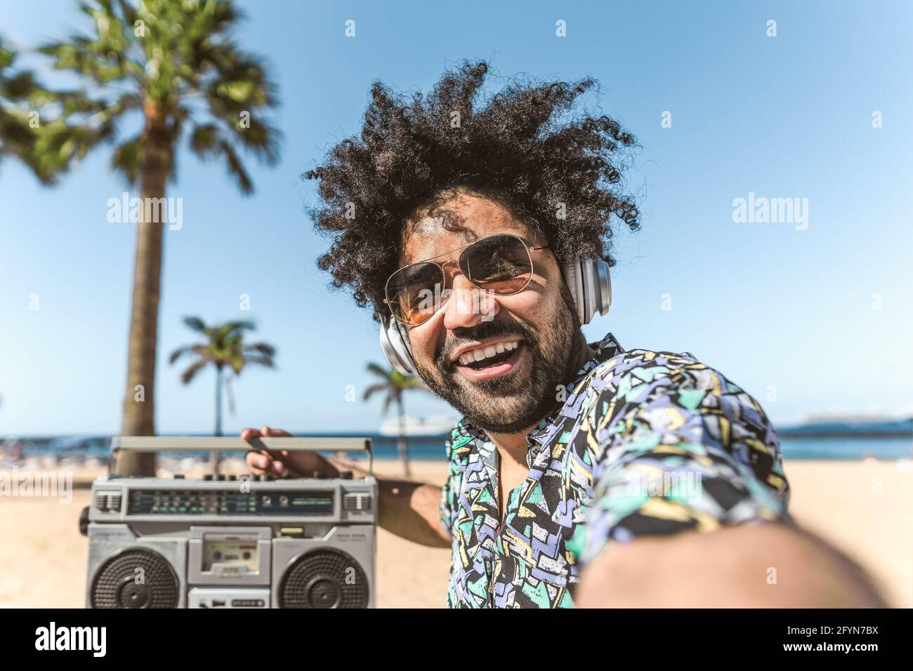 Junger Latein-Mann, der Spaß hat, Selfie mit dem mobilen Smartphone zu machen Beim Musikhören mit Kopfhörern und Boombox am Strand Während der Sommerferien Stockfoto Junger Latein-Mann, der Spaß hat, Selfie mit dem mobilen Smartphone zu machen Beim Musikhören mit Kopfhörern und Boombox am Strand Während der Sommerferien Stockfoto