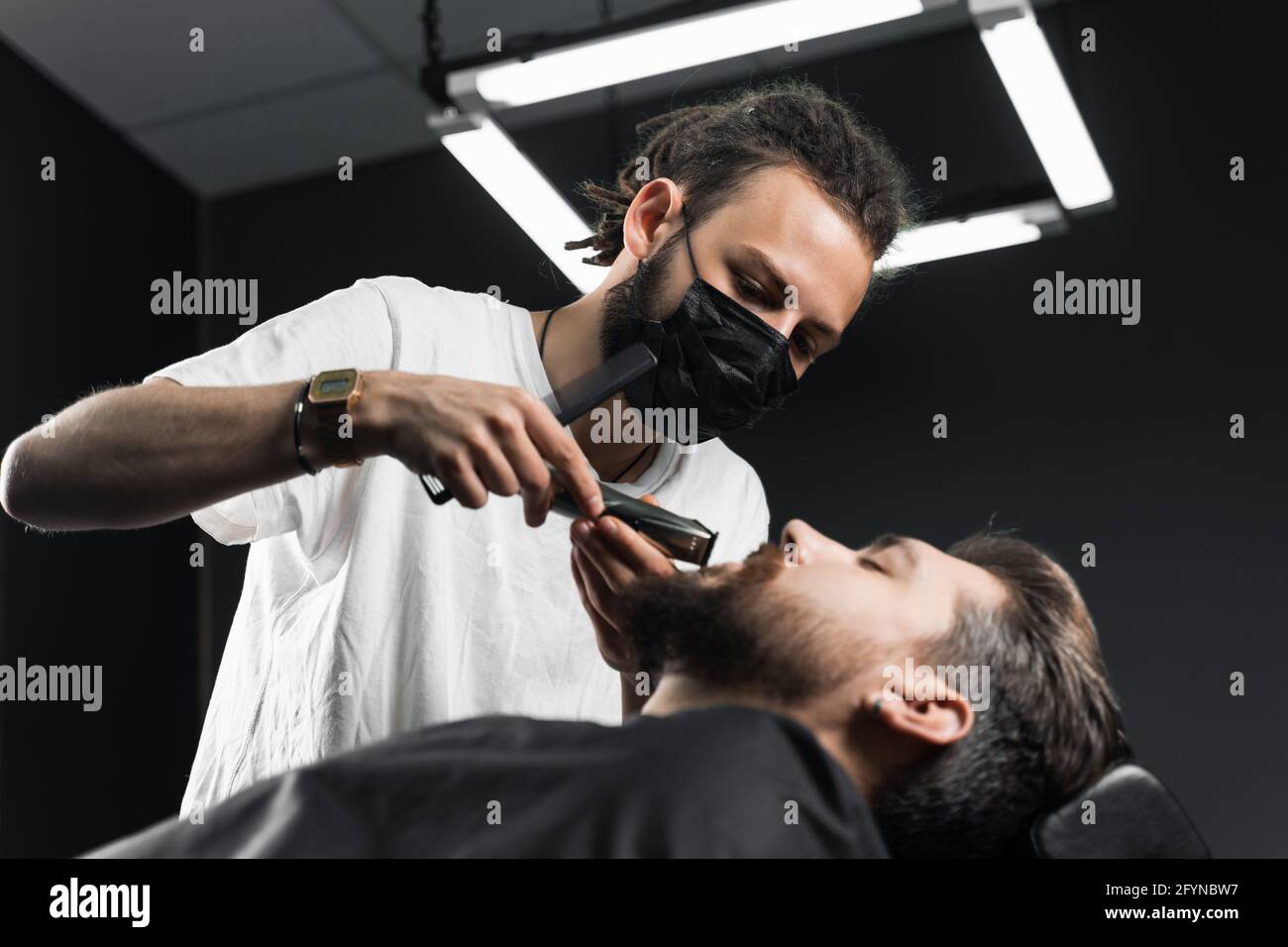 Schnurrbart rasieren im Friseurladen. Barbier mit Dreadlocks in schwarzer  medizinischer Maske trimmen den Bart eines gutaussehenden Mannes bei  Quarantäne-Coronavirus covid-19 Stockfotografie - Alamy