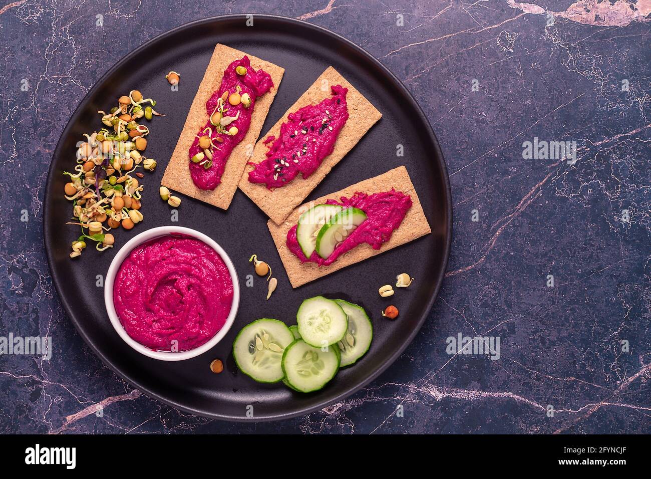 Vegetarischer, veganer Snack - Rote Beete Hummus, gekeimtes Getreide, Gurke und Vollkornknusprige. Stockfoto