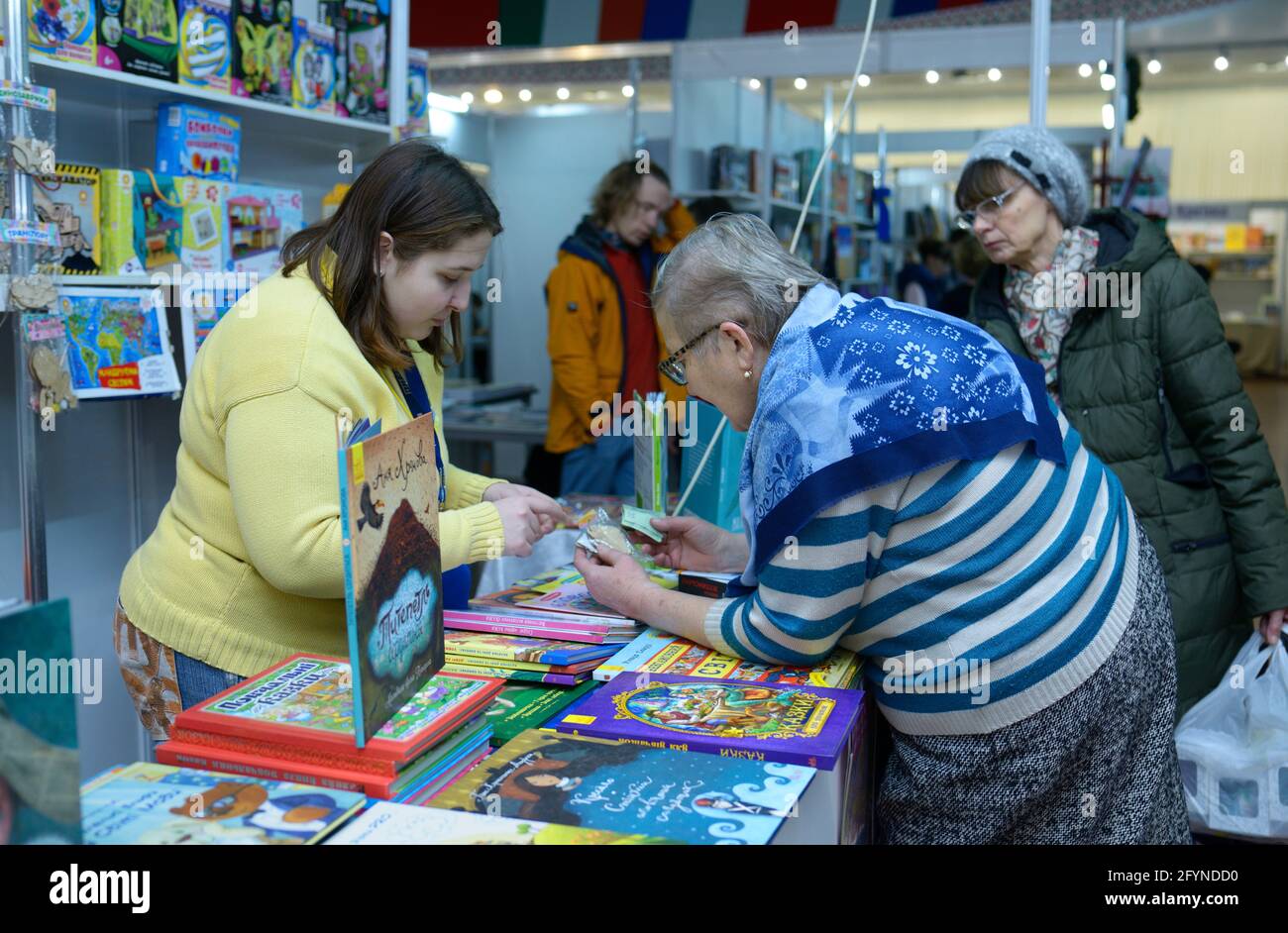 Eine alte Frau wählt das Buch zum Lesen aus, der Buchhändler steht hinter einer Theke der Buchhandlung. Buchmesse Knyzhkovyi Arsenal . 24.Mai 2019. Kiew, Ukraine Stockfoto
