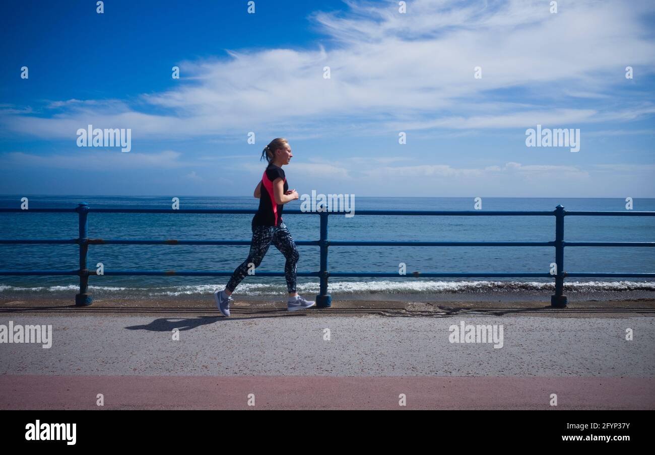 Die jüngere Joggerin läuft am Meer mit fernem Horizont Stockfoto