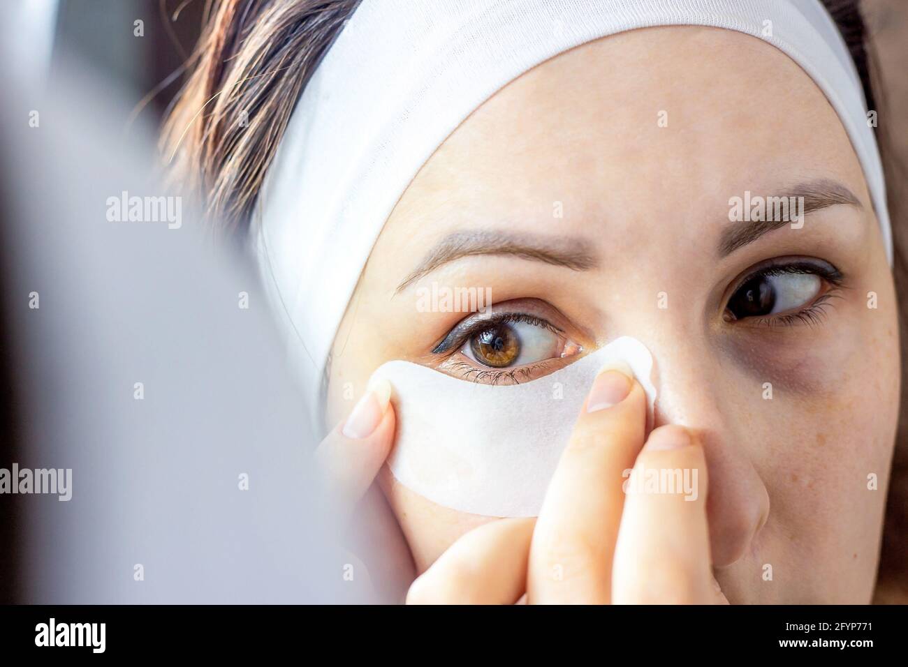 Die junge kaukasische Frau, die eine Augenmaske auf ihr Augenlid anwendet, um Falten in den Spiegel zu vermeiden. Home Hautpflege Verfahren, Beauty-Behandlung concep Stockfoto