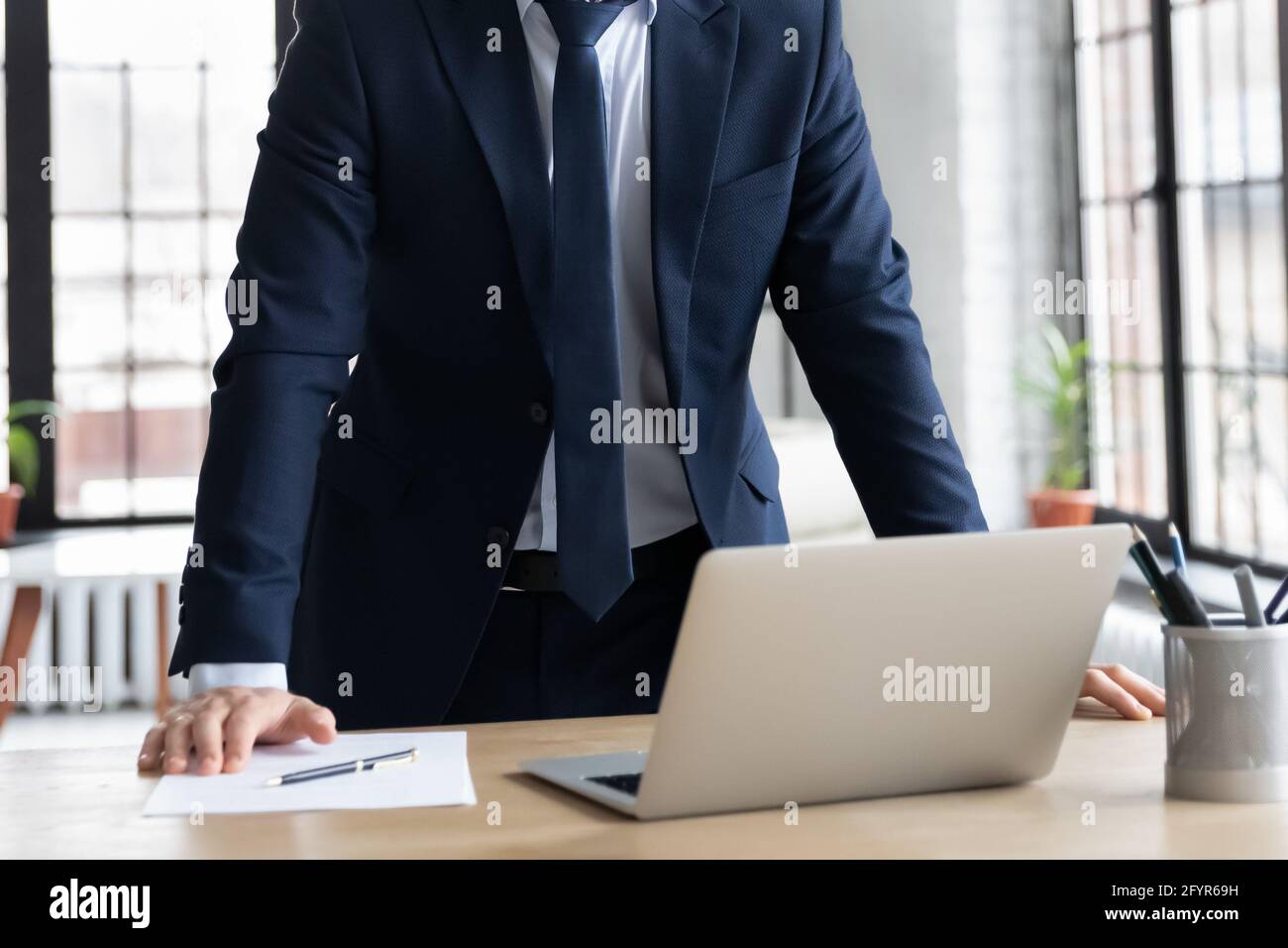 Geschäftsmann im Anzug, der mit Laptop und am Schreibtisch steht Dokument Stockfoto
