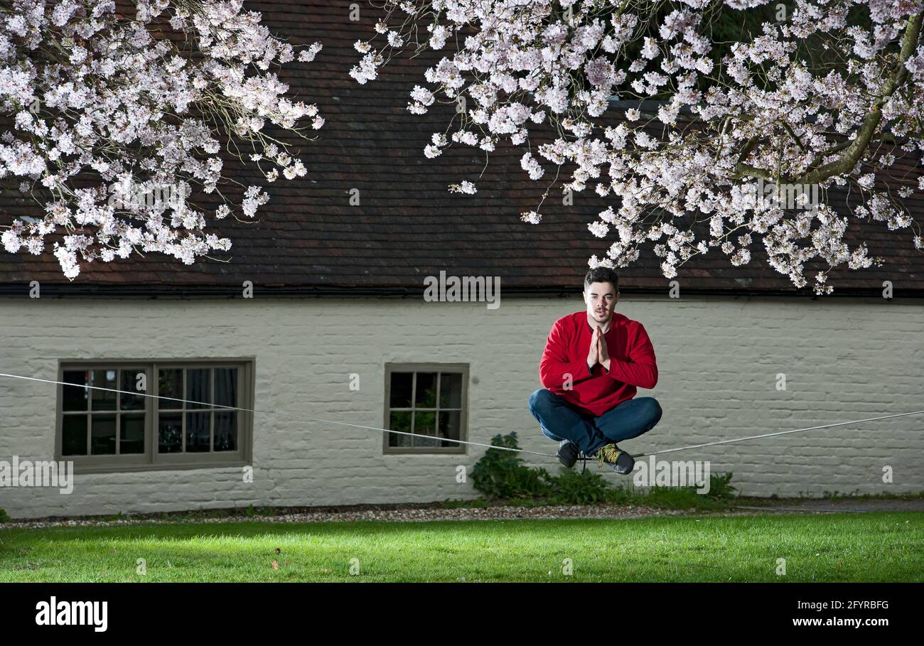 Der junge Mann übt sein Gleichgewicht auf einer schlaffen Linie zwischen zwei Bäumen Stockfoto