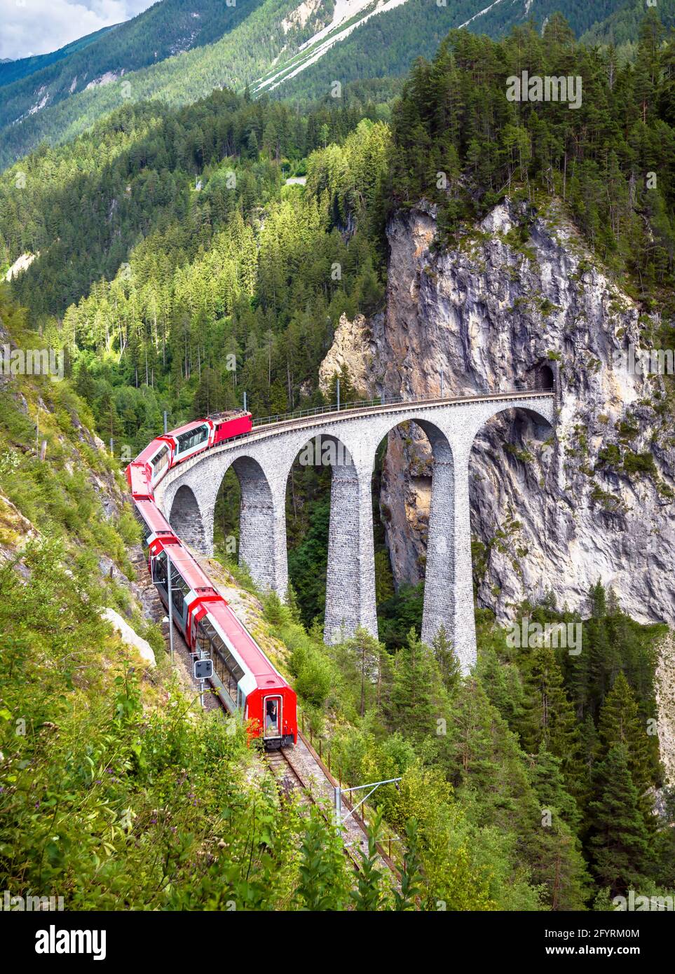 Rhätian Express bewegt sich auf dem Landwasser Viadukt, Schweiz. Dieser Ort ist das Wahrzeichen der Schweizer Alpen. Vertikale Ansicht der Eisenbahnbrücke und des roten Zuges, schön Stockfoto