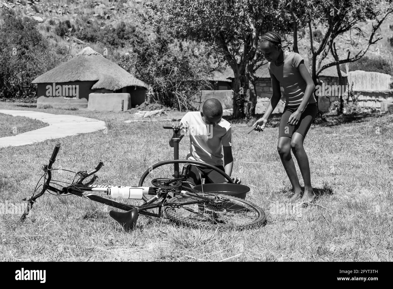 HARRISMITH, SÜDAFRIKA - 05. Jan 2021: Harrismith, Südafrika - 18 2012. Oktober: Afrikanische Kinder, die eine Punktion auf einem Fahrrad reparieren Stockfoto