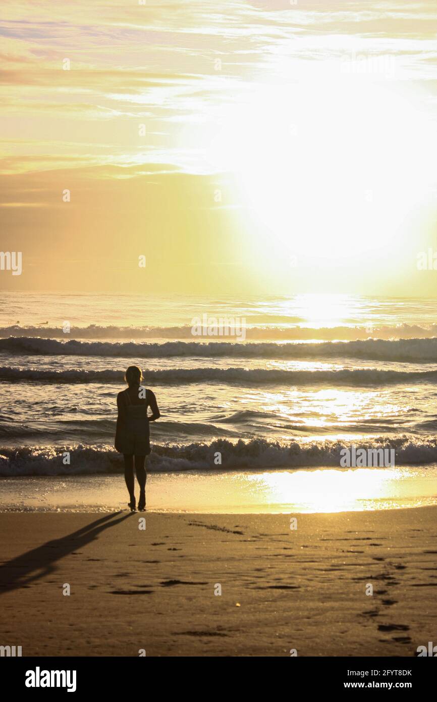 Eine Silhouette einer Person, die am Strand bei Beautiful steht Gelber Sonnenuntergang Stockfoto
