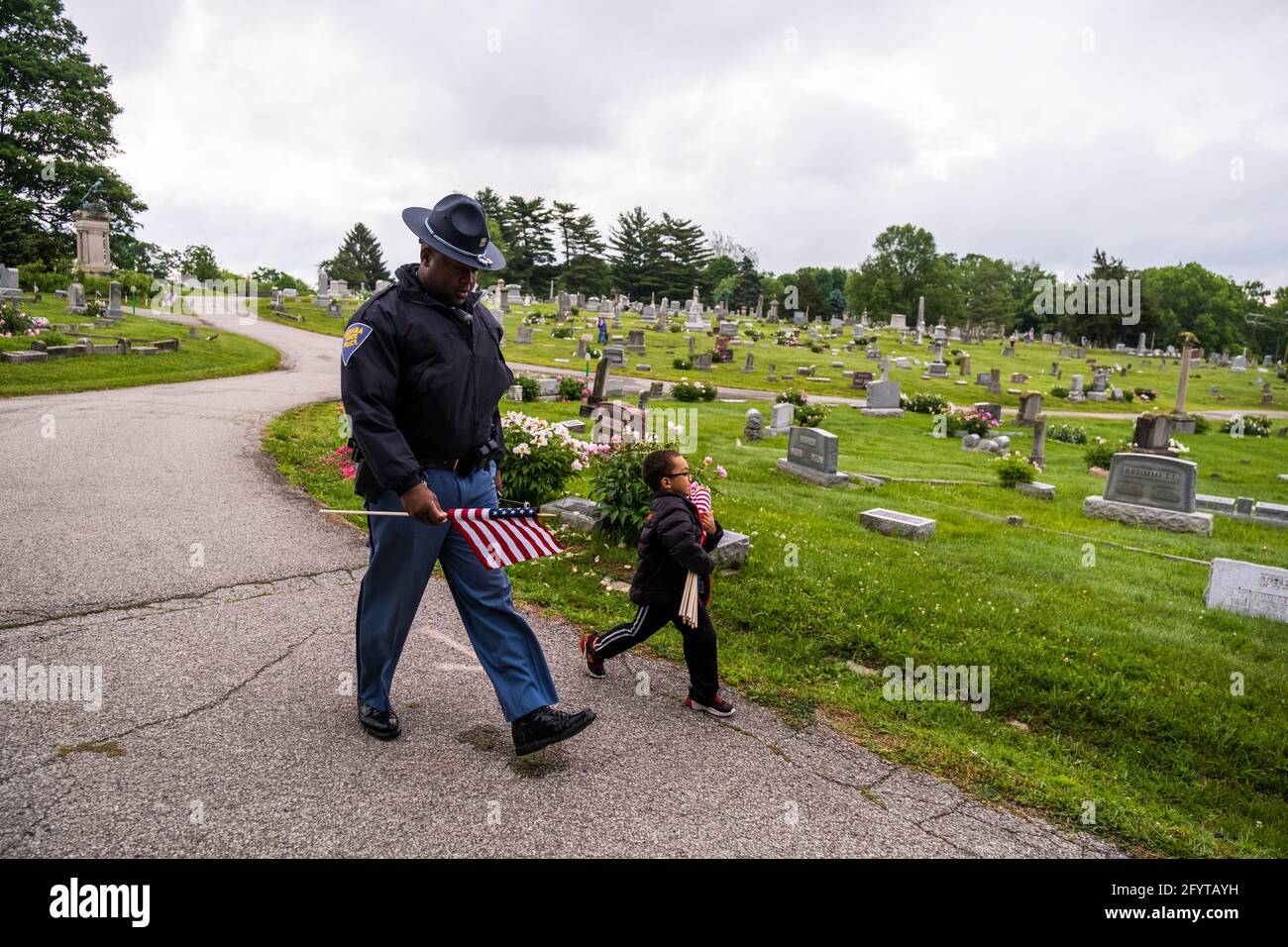 Bloomington, Usa. Mai 2021. Indiana State Trooper Matt Harris, links, und sein Sohn Dominic Harris, von Cub Scouts Pack 145, tragen Flaggen, um auf die Gräber von Veteranen auf dem Rose Hill Friedhof am Memorial Day Samstag zu platzieren. Memorial Day, der Montag, den 31. Mai dieses Jahres, ist ein Bundesfeiertag für die Ehre der Mitglieder der Streitkräfte der Vereinigten Staaten, die während der Ausübung ihrer Pflichten gestorben sind. Kredit: SOPA Images Limited/Alamy Live Nachrichten Stockfoto