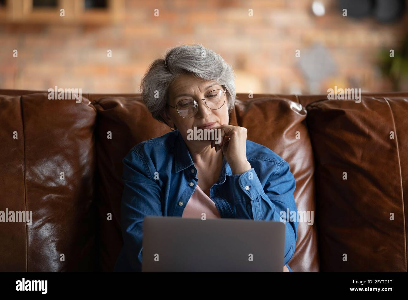 Durchdachte, reife Frau, die mit einem Laptop auf dem Sofa sitzt Stockfoto