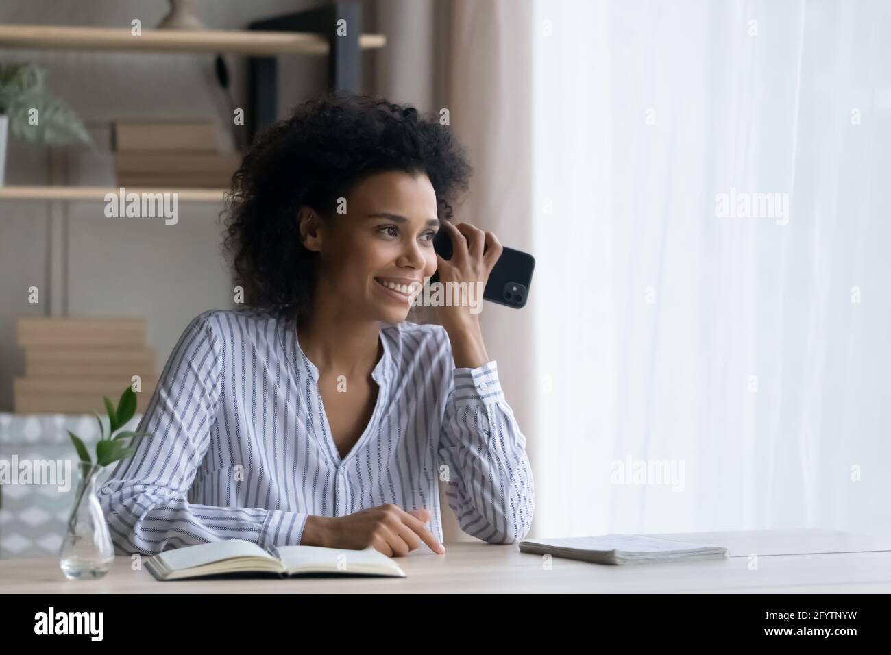 Glückliche Birazialfrau hört sich Audiobotschaft auf dem Handy an Stockfoto