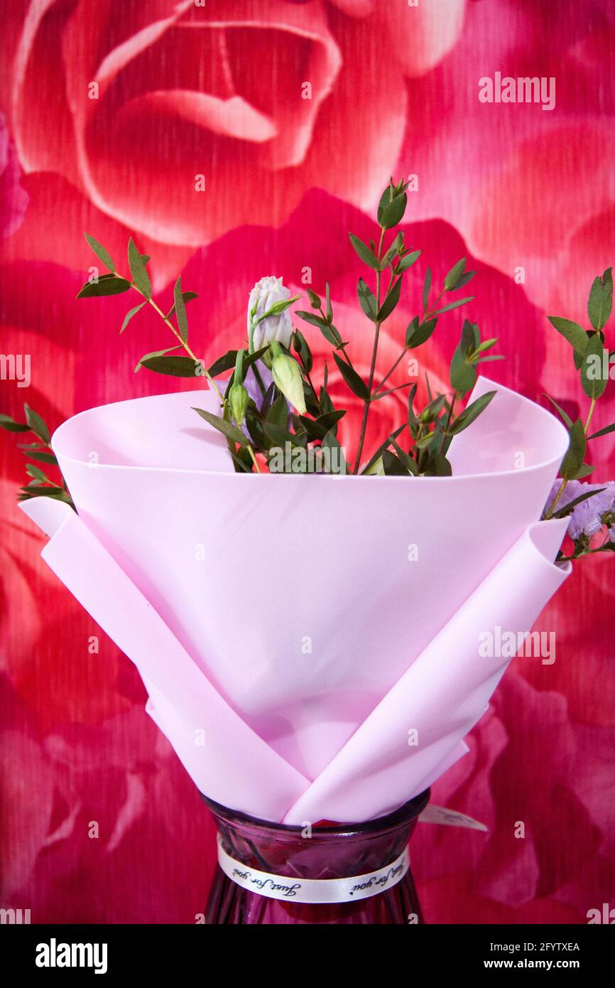 Ein zartes Blumenstrauß mit verschiedenen Blumen in einem hellrosa Wrapper steht in einer häuslichen Umgebung gegen eine bunte rosafarbene Wand. Vertikales Foto. Stockfoto