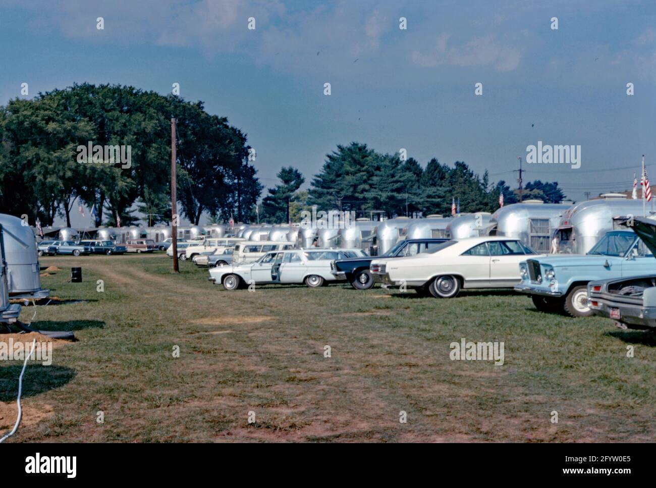 Eine Versammlung oder Kundgebung auf einem Campingplatz mit kultigen Airstream-Wohnwagen in den USA c. 1970. Der Airstream Caravan (Reiseanhänger) hat eine unverwechselbare abgerundete Form und eine Karosserie aus poliertem Aluminium. Diese Form stammt aus den 1930er Jahren und basiert auf dem Bowlus Road Chief, einem früheren Anhänger, der von Hawley Bowlus entworfen und gebaut wurde. Airstream-Anhänger und Freizeitfahrzeuge werden in Jackson Center, Ohio, USA, hergestellt. Dieses Bild stammt aus einer alten amerikanischen Kodak Amateur-Farbtransparenz – einem Vintage-Foto aus den 1960er/70er Jahren. Stockfoto