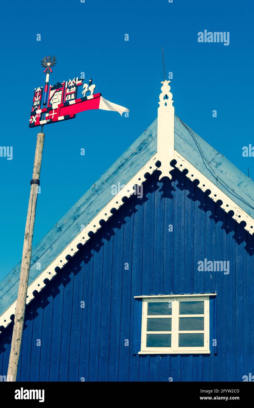 Schöner, farbenfroher Wetterhahn, der in der Kurischen Nehrung im Fischerdorf Nida, Litauen, Europa, winkt, mit blauem Himmel und Dach eines blauen Holzhues Stockfoto