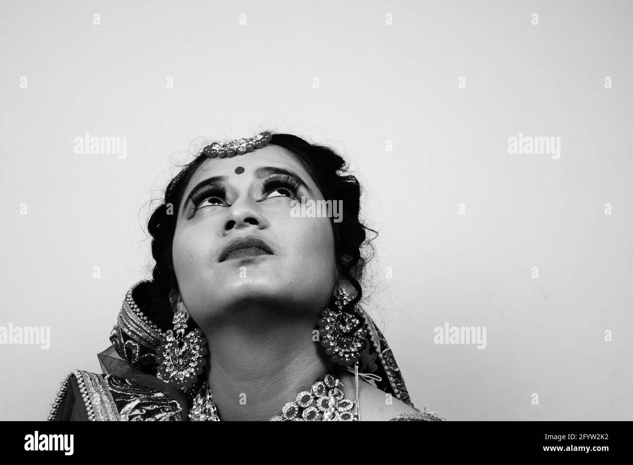 Eine Graustufenaufnahme einer jungen Inderin, die eine trägt Traditionelles Sari-Kleid und Schmuck zum Aufschauen Stockfoto