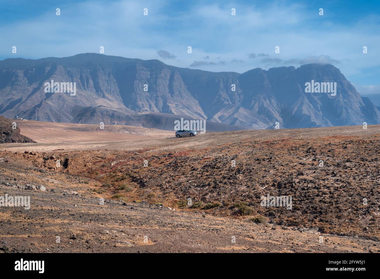 Ein Auto fährt in Galdar eine Wüstenstraße entlang Die Tamadaba Berge im Hintergrund Stockfoto