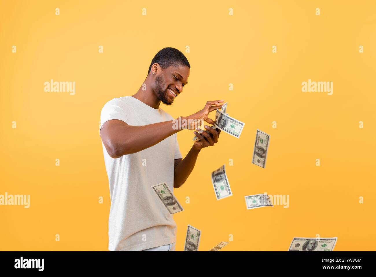 Wohlstandskonzept. Junger reicher schwarzer Kerl, der Geldscheine auswirft und über gelbem Studiohintergrund steht Stockfoto