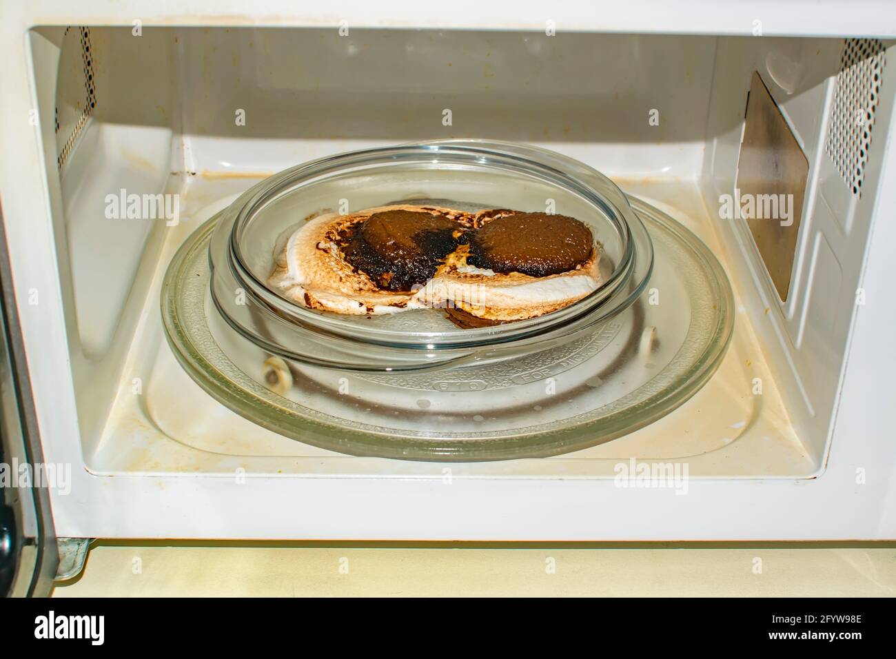 Ein geschmolzenes Brötchen, verbrannt zu Glut, liegt auf einem Teller in der Mikrowelle. Verdorbenes Essen, Süßigkeiten Stockfoto