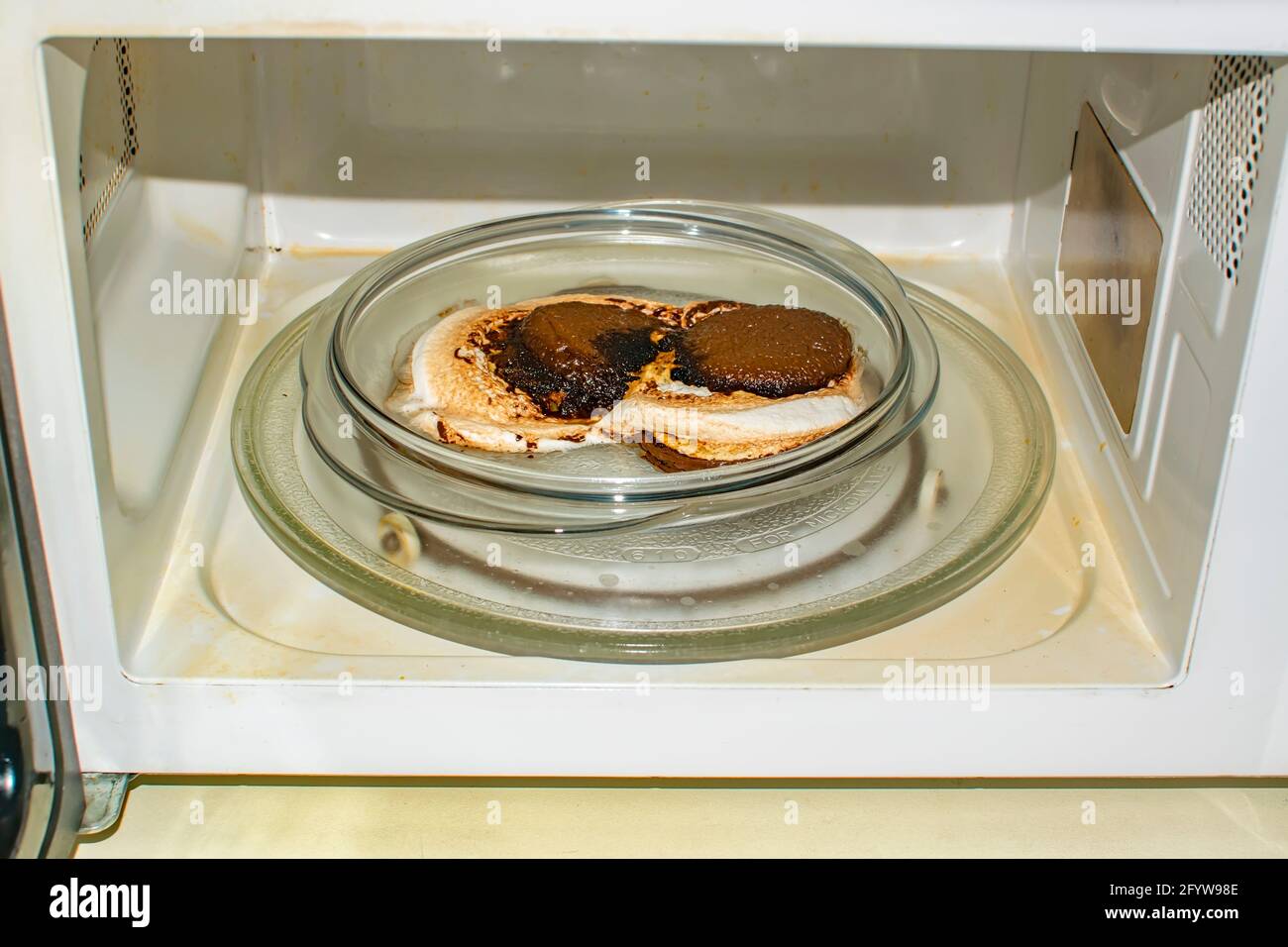 Ein geschmolzenes Brötchen, verbrannt zu Glut, liegt auf einem Teller in  der Mikrowelle. Verdorbenes Essen, Süßigkeiten Stockfotografie - Alamy