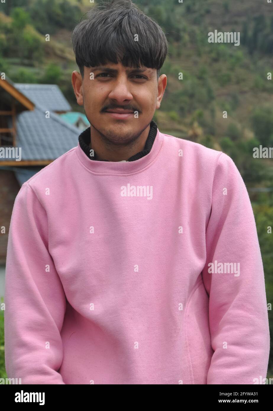 Porträt eines gut aussehenden jungen Mannes mit rosa Sweatshirt, EINES hübschen nordindischen jungen Mannes, der draußen mit Blick auf die Kamera steht Stockfoto