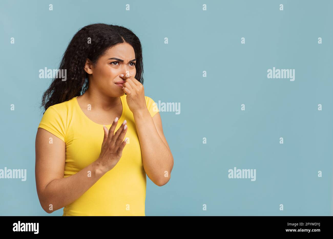 afroamerikanische Frau verstopfte ihre Nase, riecht etwas stinkend und unangenehm auf blauem Hintergrund, kopieren Raum Stockfoto