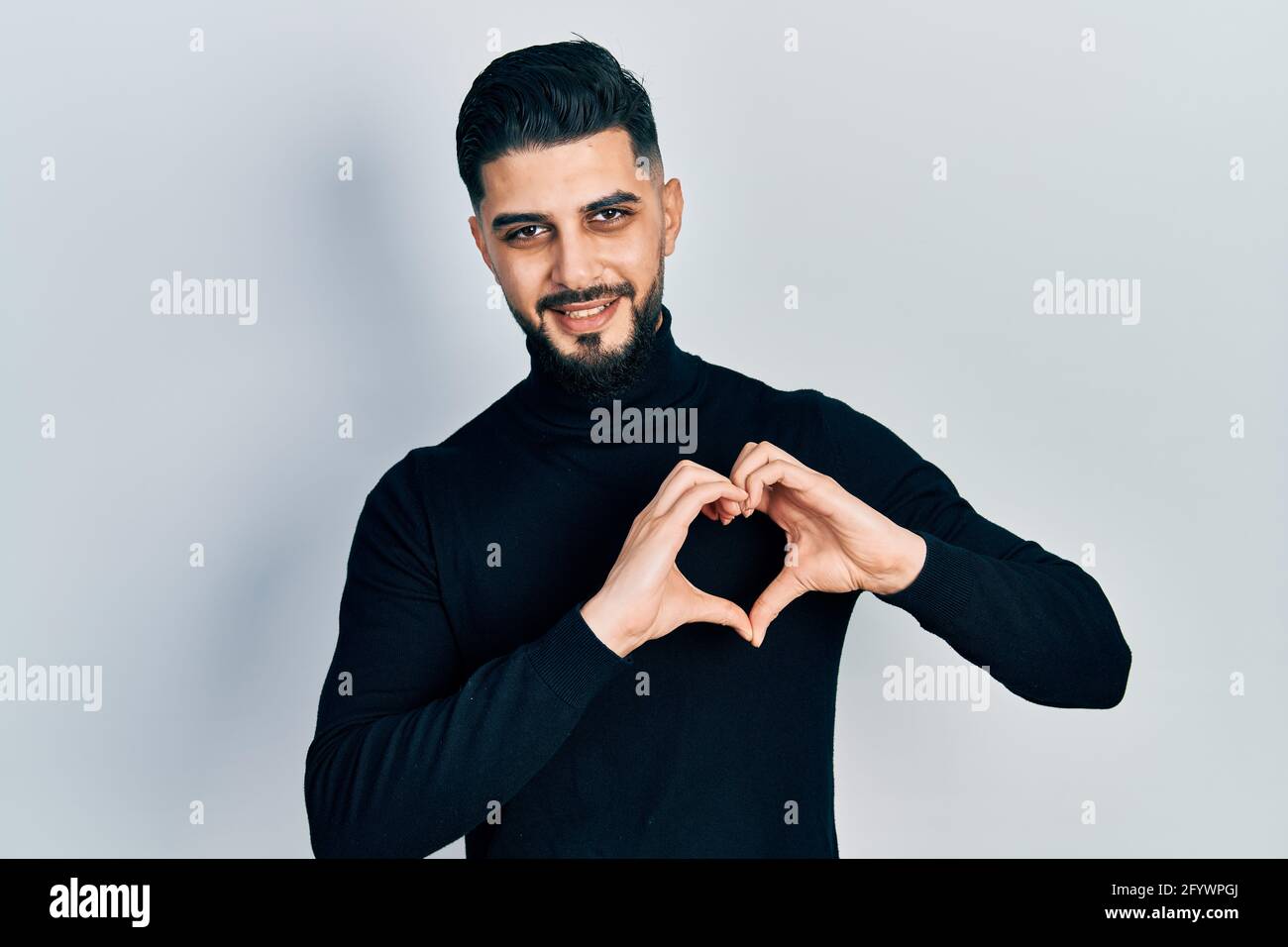 Schöner Mann mit Bart trägt Rollkragenpullover lächelnd in Liebe tun Herz Symbol Form mit Händen. Romantisches Konzept. Stockfoto