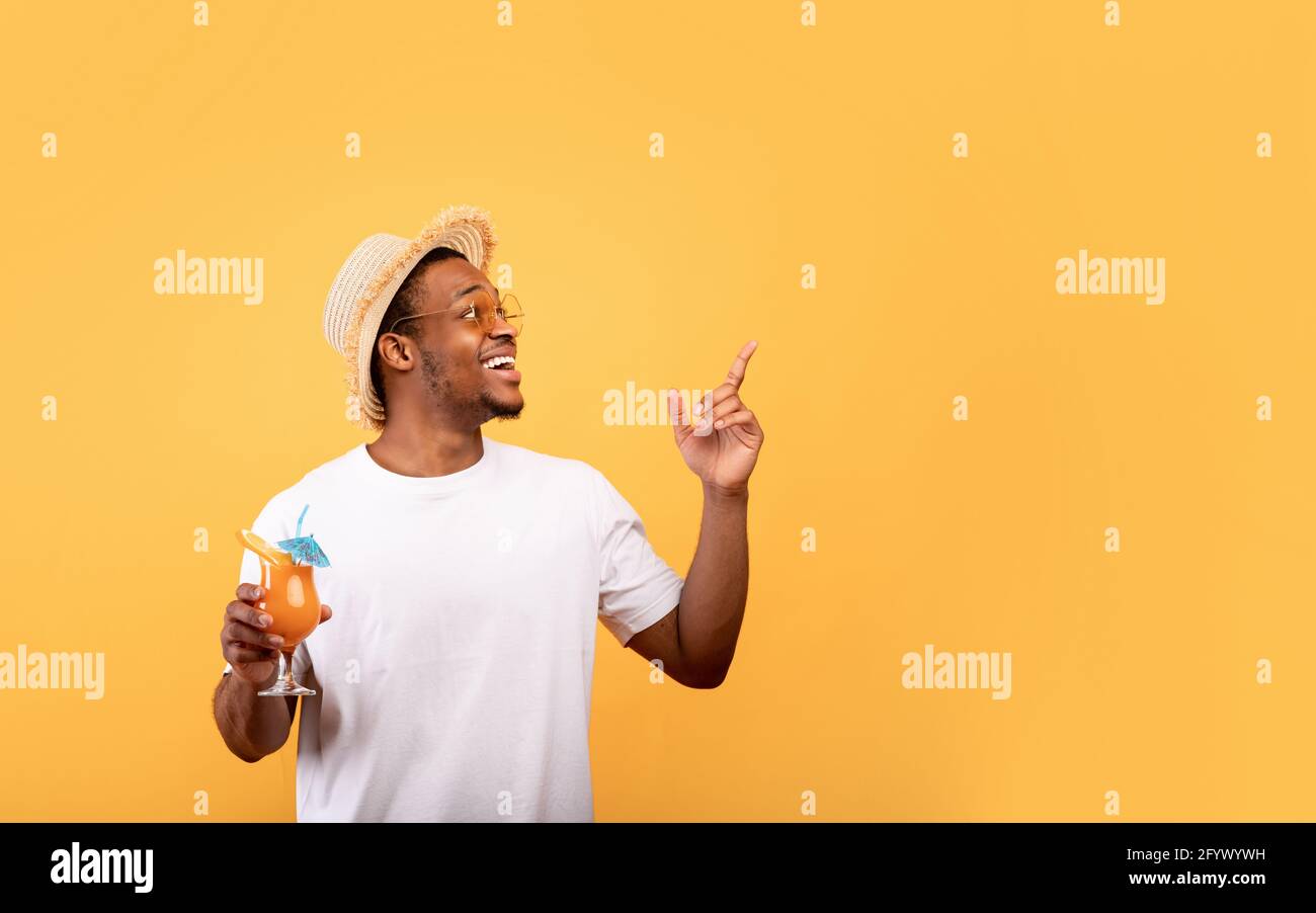 Tolles Sommerangebot. Fröhlicher afroamerikanischer Mann mit einem leckeren tropischen Cocktail, der auf leeren Raum zeigt Stockfoto