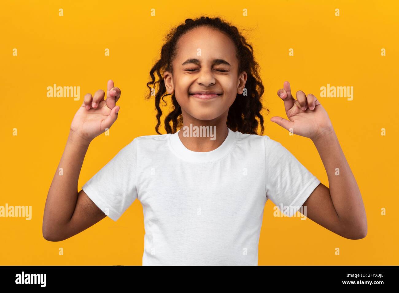 Hoffnungsvolles afroamerikanisches Mädchen, das ihre Finger kreuzt und Wunsch macht Stockfoto