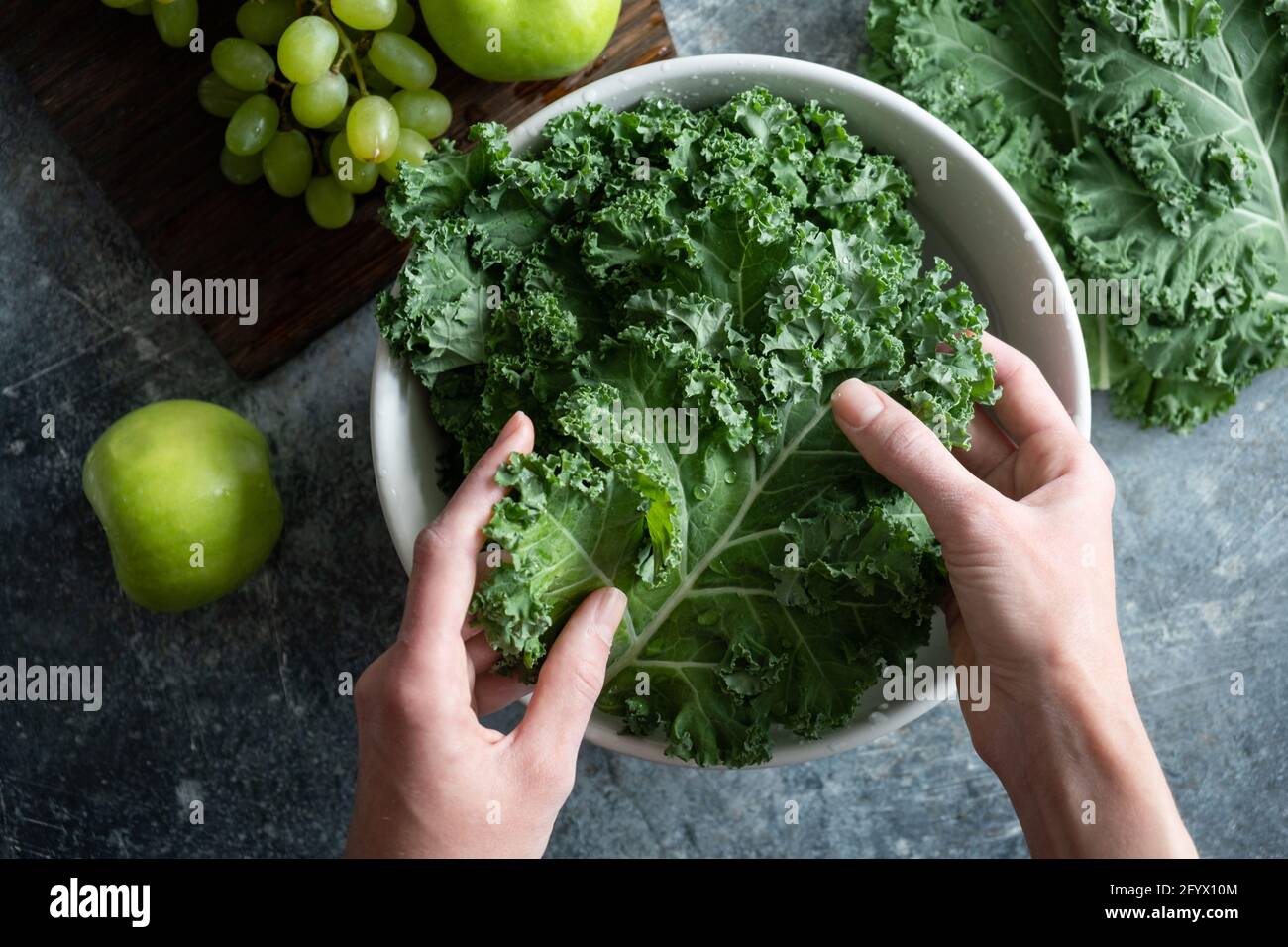 Weibliche Hände waschen Grünkohl in einer Schüssel mit Wasser. Kochen gesundes Bio-hausgewachsenes veganes Essen, Draufsicht Stockfoto