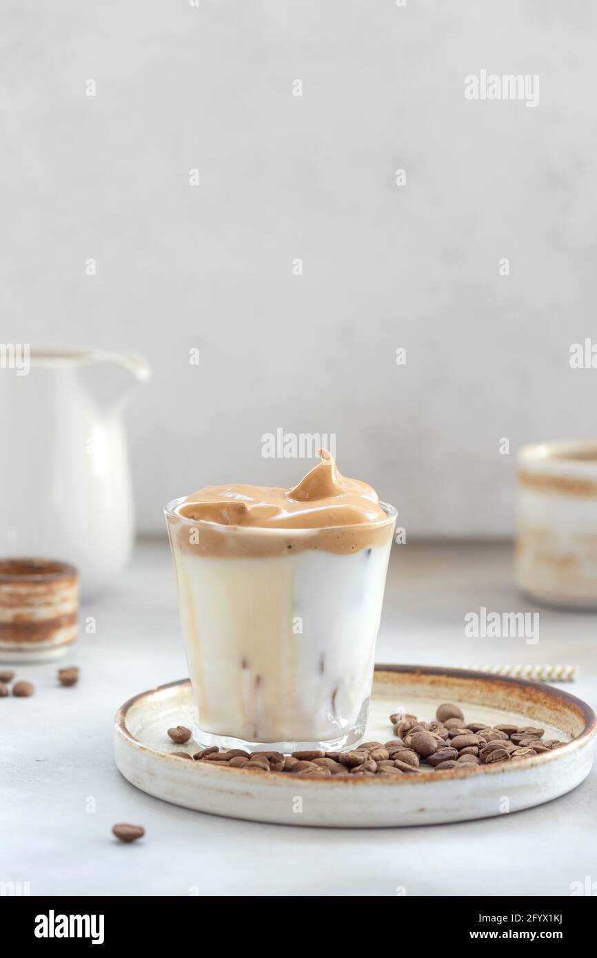 Iced Dalgona Kaffee mit flauschigen süßen Schaum in einem Glas auf einem grauen Hintergrund. Trendigen Sommergetränk. Vertikales Bild. Raum kopieren. Stockfoto