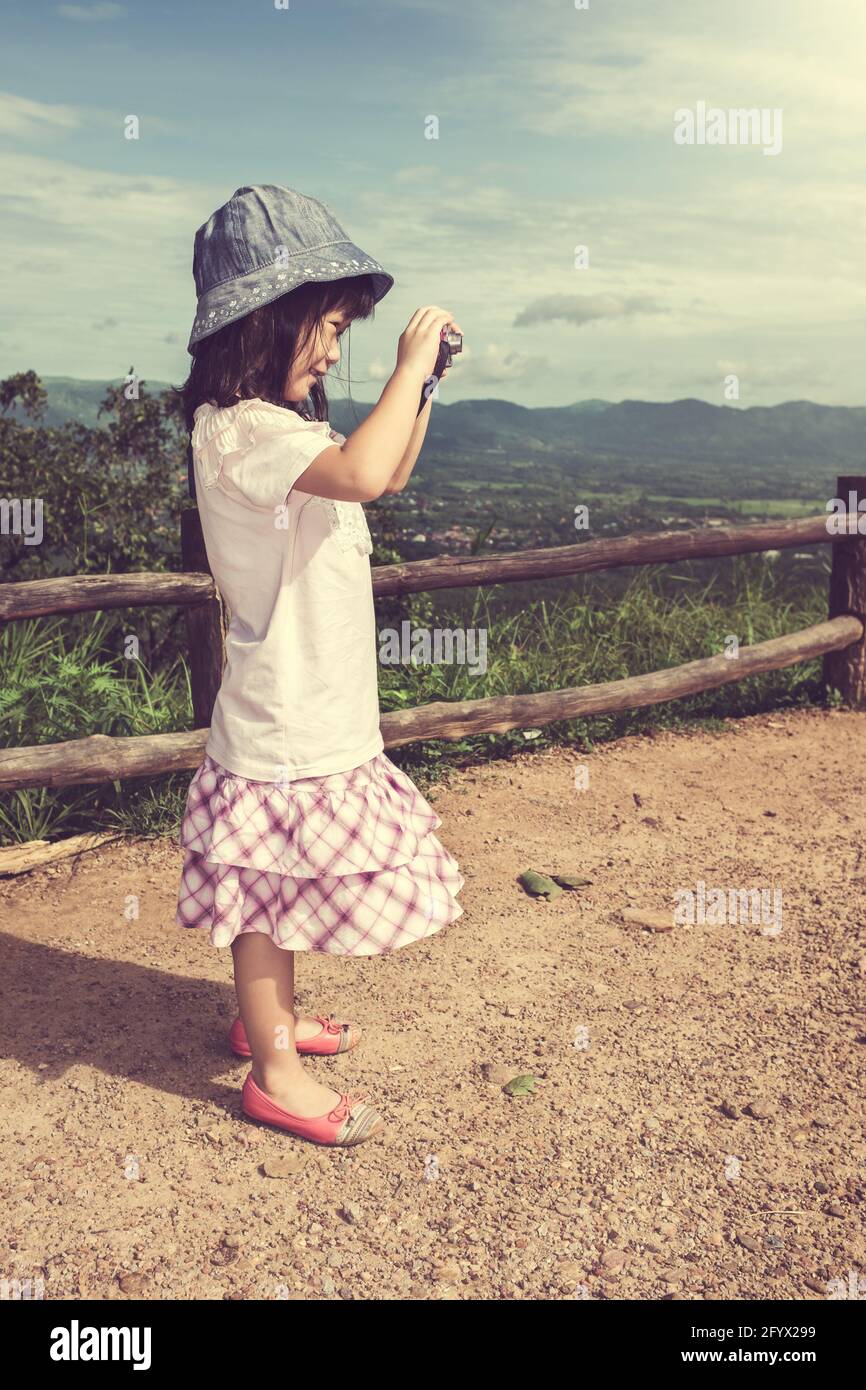 Seitenansicht des glücklichen asiatischen Mädchen lächeln am Aussichtspunkt auf Berg und lernen fotografieren Natur mit der Kamera. Kinder entspannen sich tagsüber im Freien Stockfoto