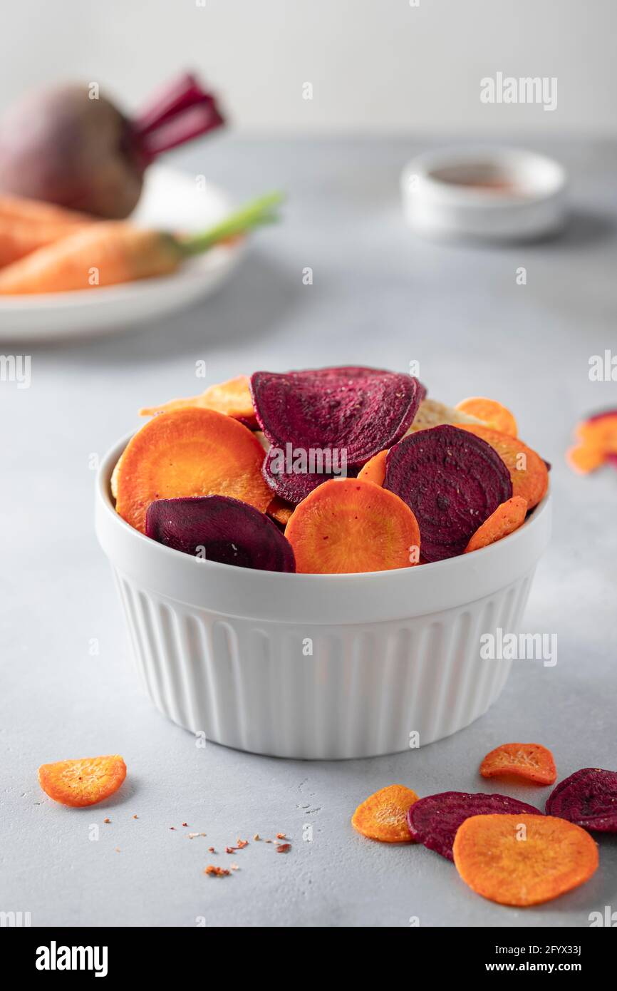 Schüssel mit gemischten gesunden Gemüsechips aus Rüben und Karotten auf grauem Hintergrund. Getrocknetes Gemüse. Vertikales Bild. Stockfoto
