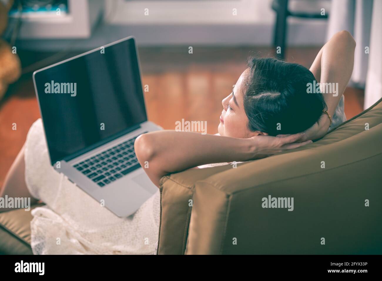 Schöne asiatische Frau ruht und umklammert ihre Hände hinter ihrem Nacken mit geschlossenen Augen nach der Arbeit hart mit Laptop-Computer, Seitenansicht. Stockfoto